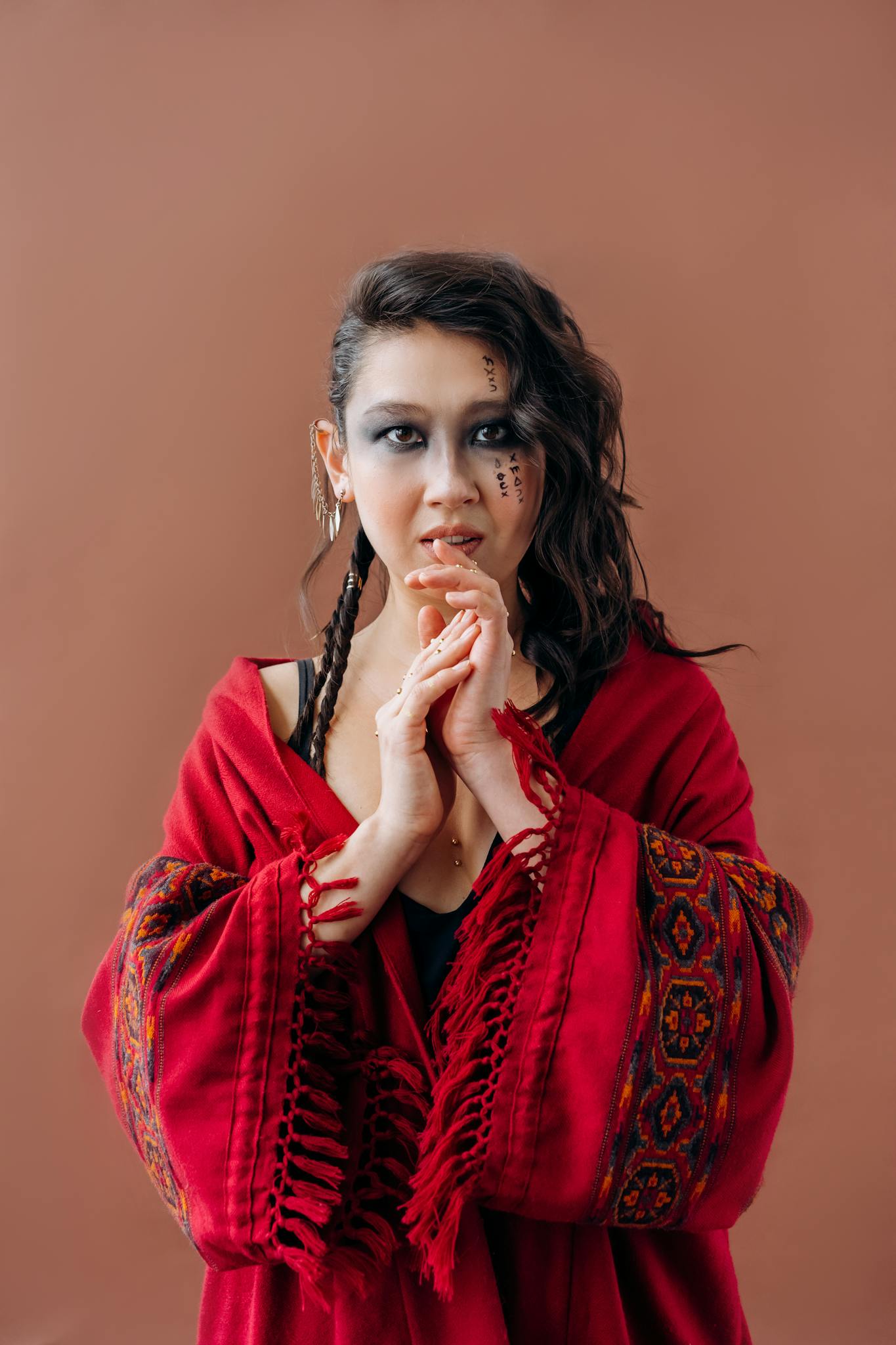 A woman in a red shawl with intricate patterns poses against a neutral background.